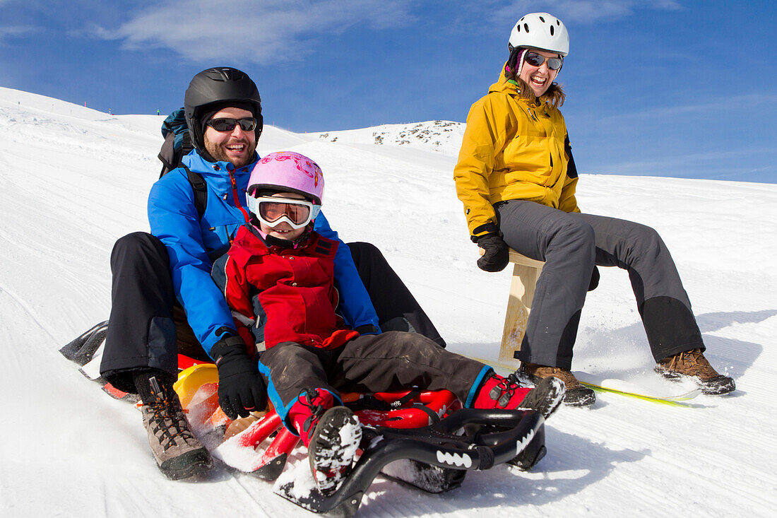 Eine Familie, Vater, Mutter, kleine Tochter beim Schlittenfahren auf der Schlittelbahn im Wintersportgebiet Stoos mit dem modernen Schlitteln Scorpion Racer, Kanton Schwyz, Schweiz