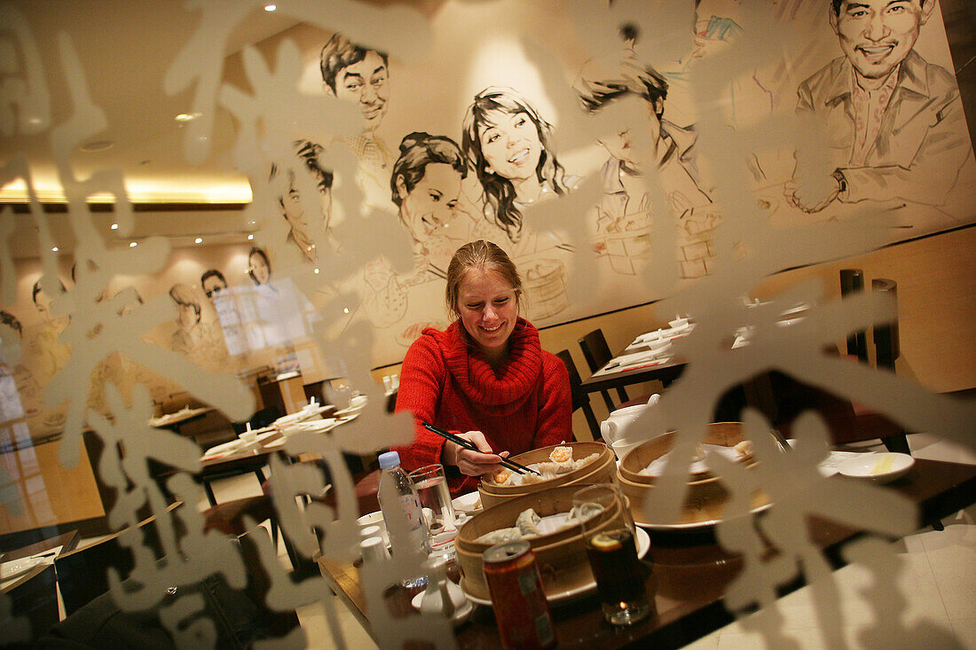 Woman eating dumplings with chopsticks at Din Tai Fung Dumpling House, Xintiandi (XinTianDi), Shanghai, China