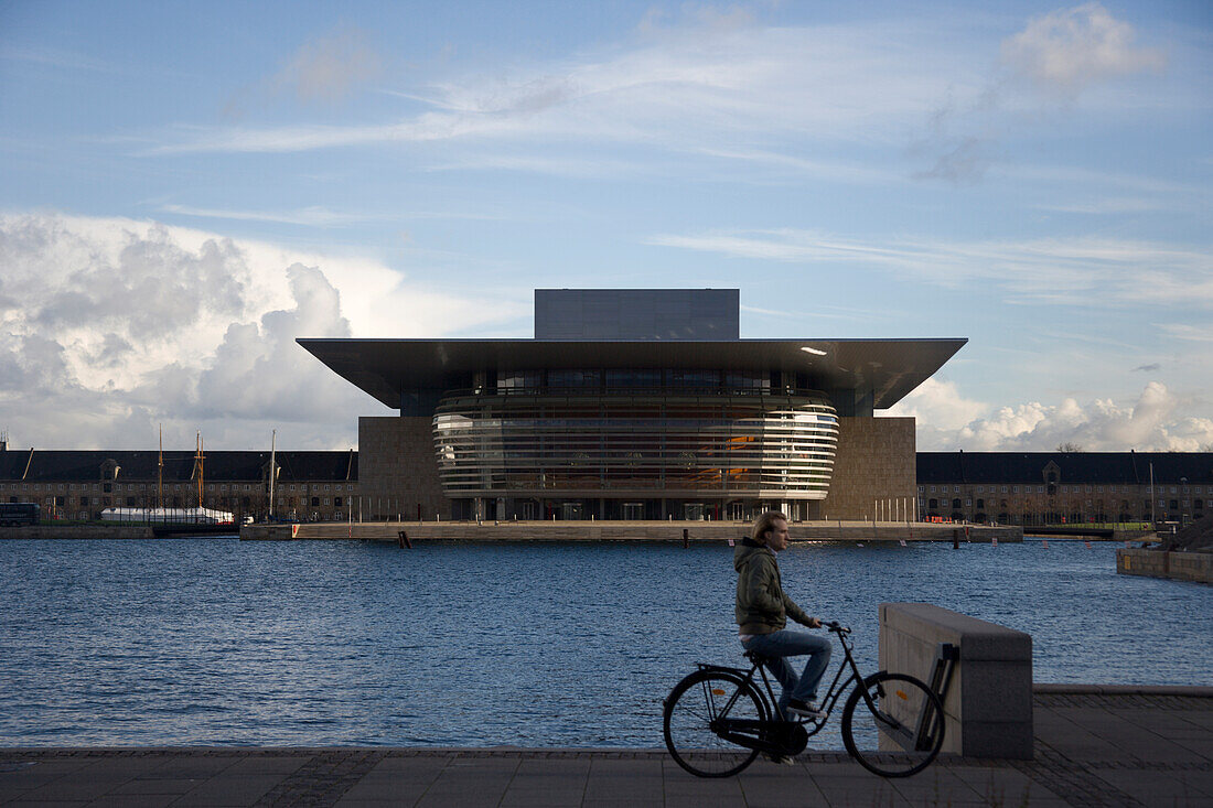 Man riding bicycle with Opera building in background, Copenhagen, Denmark