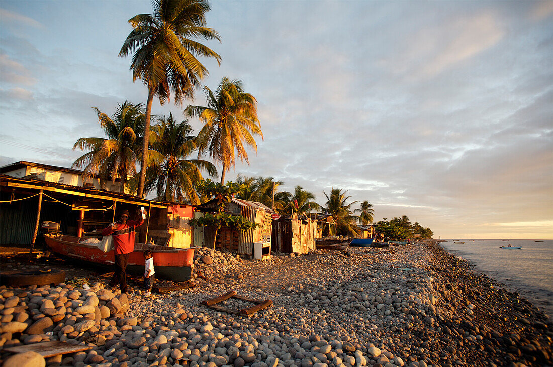 People in front of shacks on beach at sunset, Roseau, Dominica