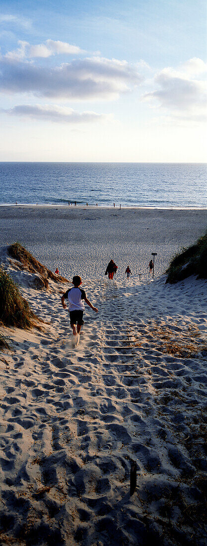 Boy running through path in sand dunes towards sea, Holmsland Klit, West Jutland, Denmark