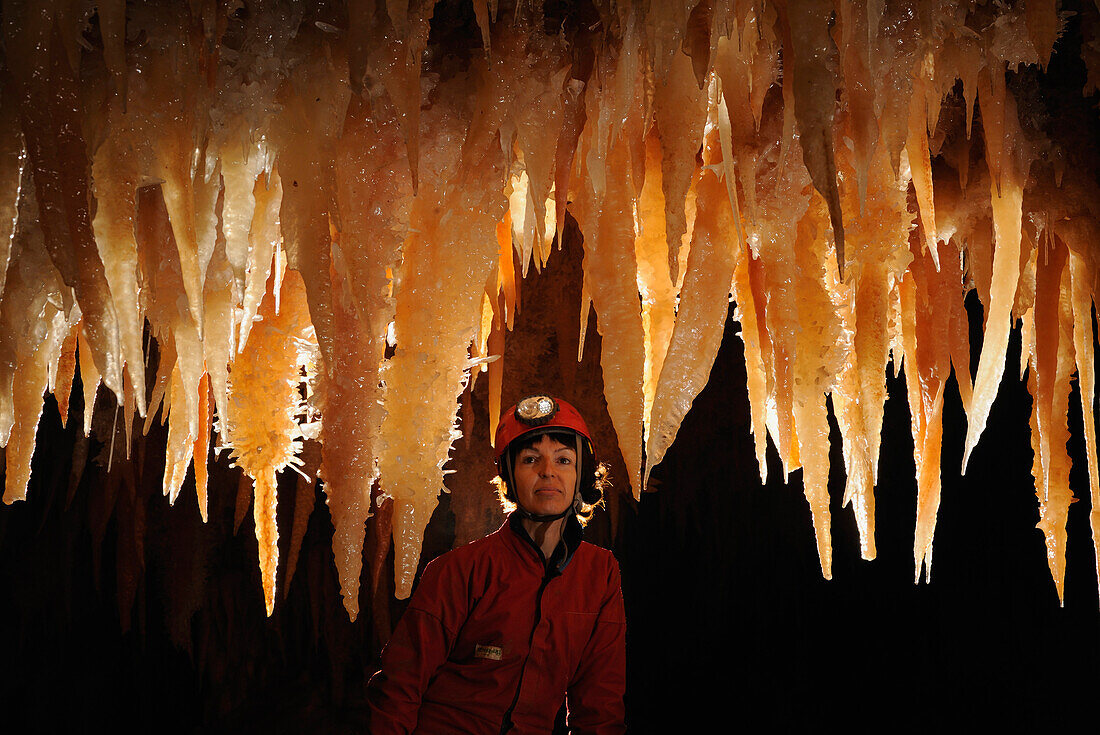 Speleology, caving, caver looking at big orange stalactites