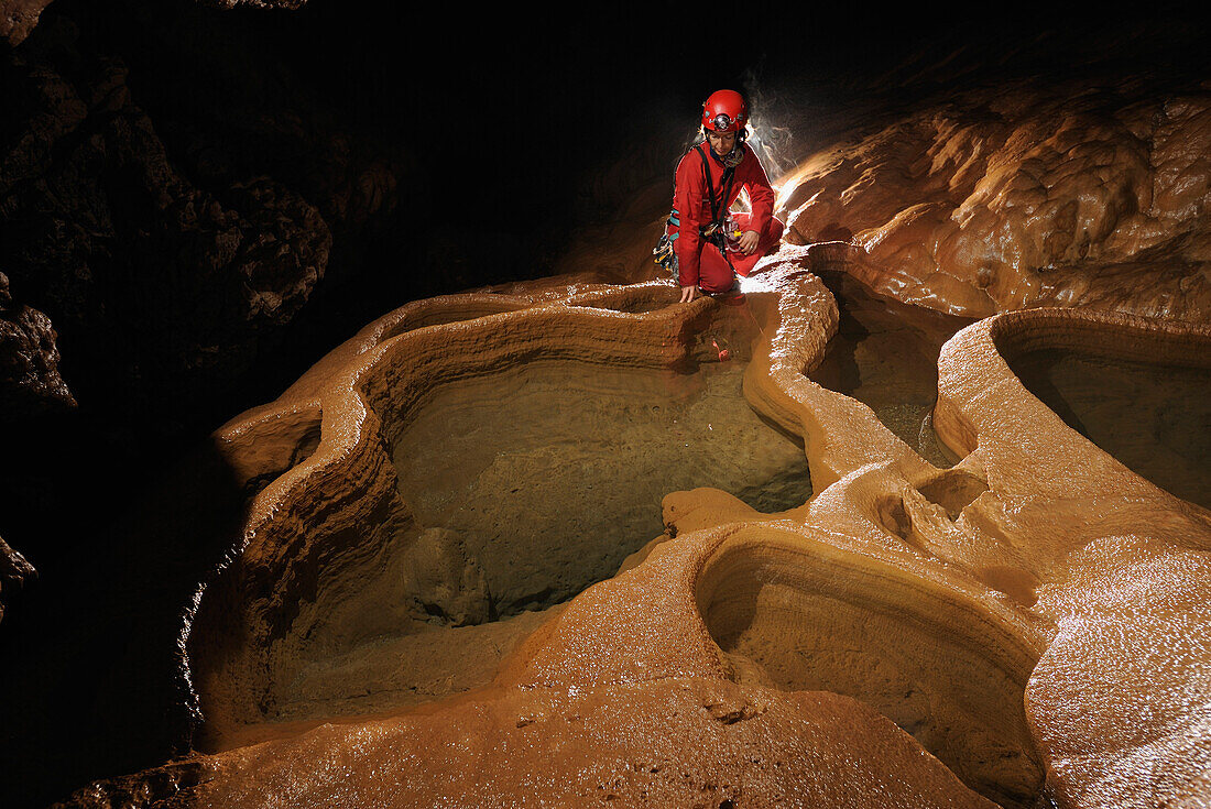 Speleology, caving, caver above large rimstone pool full of water