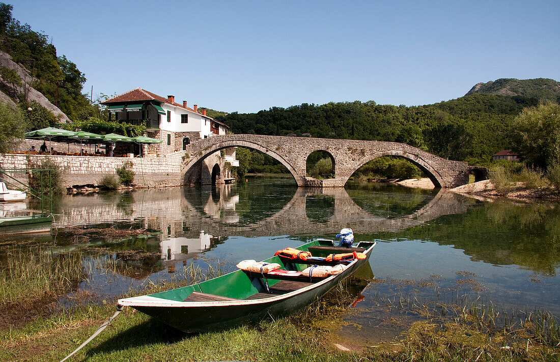 Boats on river at Rijeka Crnojevica, tributary of Lake Skadar, with old stone bridge in distance, Montenegro