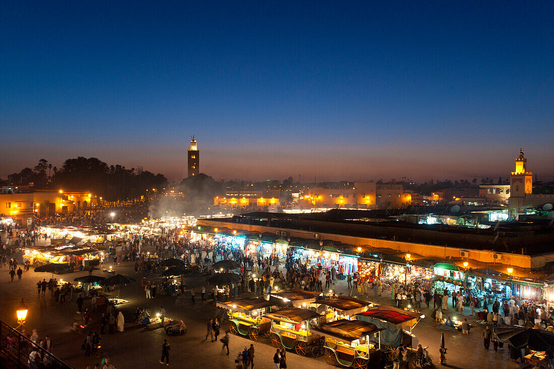 Food stalls in Djemaa El Fna with the Koutoubia minaret in the background at dusk, Marrakesh, Morocco
