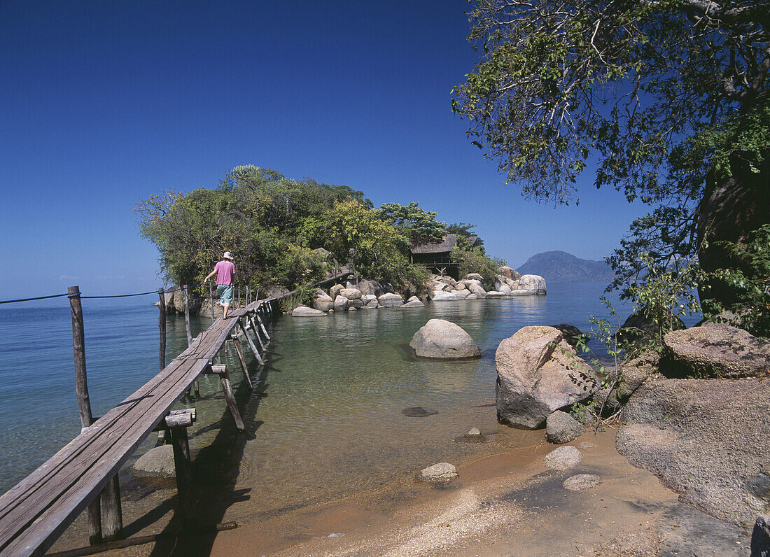 Woman walking across bridge to small island off Mumbo Island, Lake Malawi, Malawi