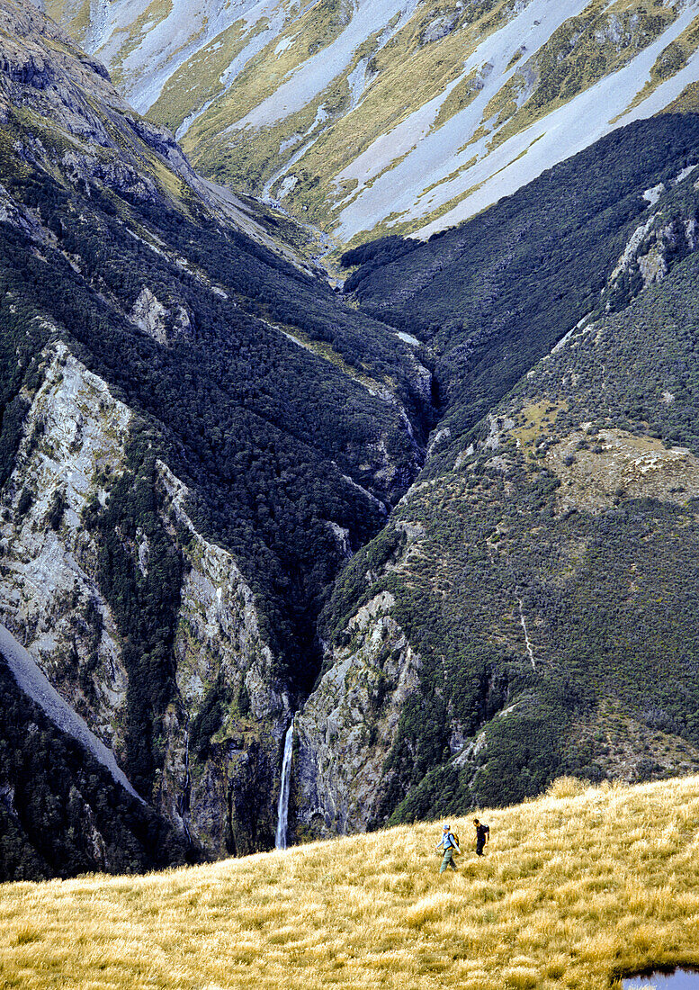 Two hikers walking in mountains, Devil's Punchbowl Waterfall, Southern Alps, South Island, New Zealand