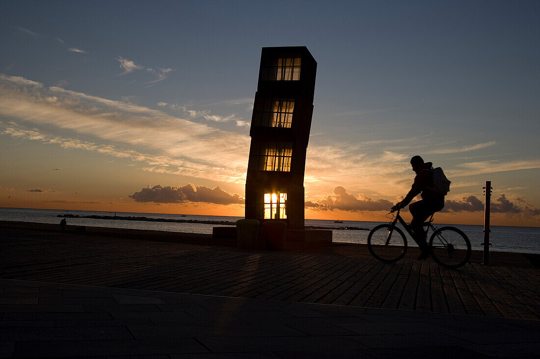 Silhouette of cyclist passing sculpture, Barcelona, Catalonia, Spain