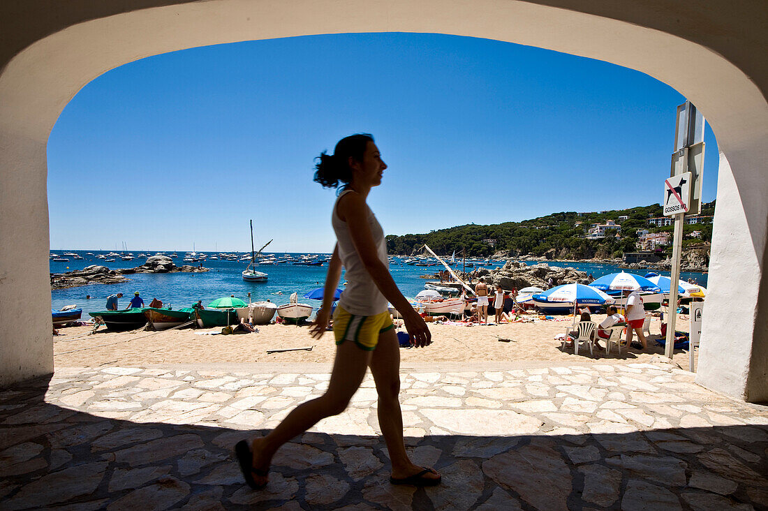 Girl walking under arch near beach in Calella fishing village, Costa Brava, Catalunya, Spain