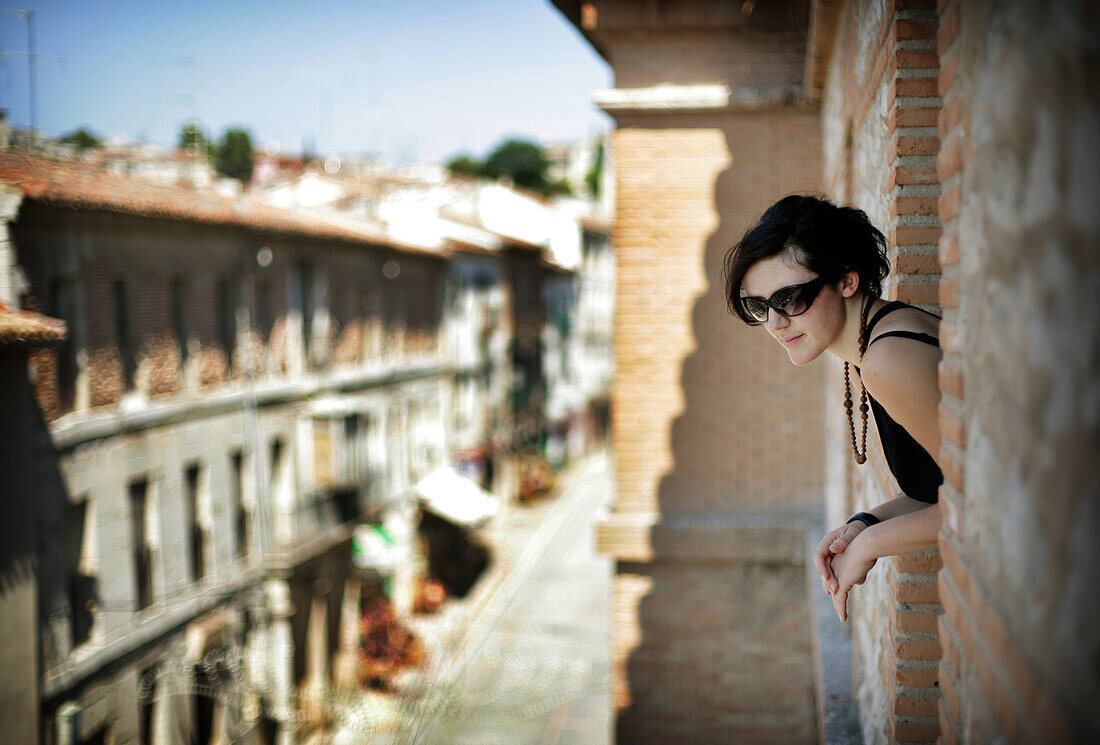 Young woman looking out of balcony window in Parador Hotel, Chinchon, Spain