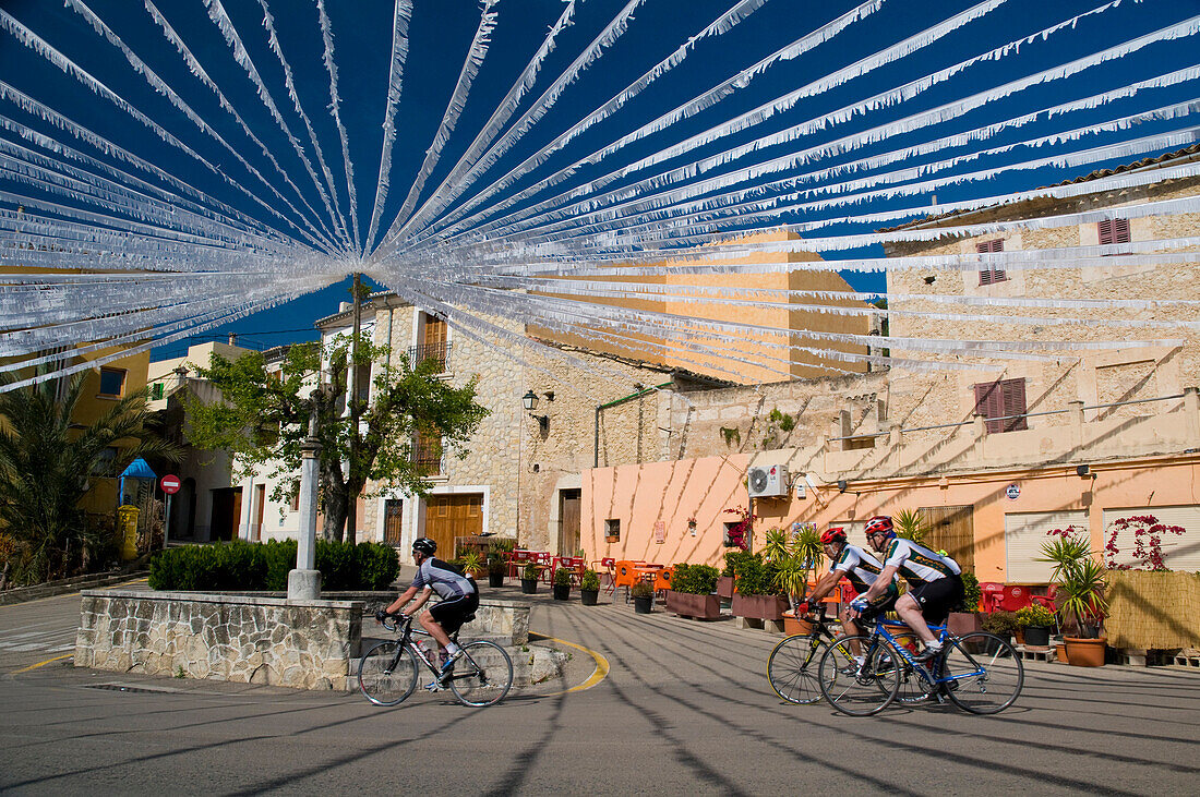 Cyclists going past square with white bunting in Caimari, Majorca, Spain
