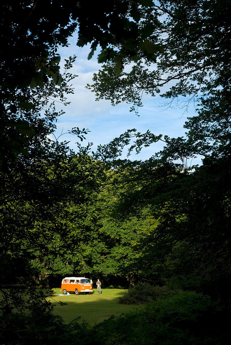Woman outside campervan in clearing in forest, New Forest, Hampshire, UK