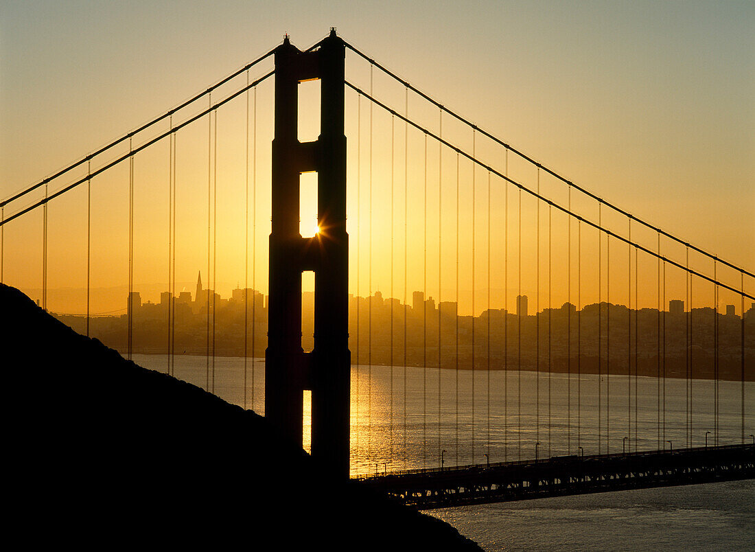 Yellow sunrise behind the Golden Gate Bridge with skyline behind, San Francisco, California