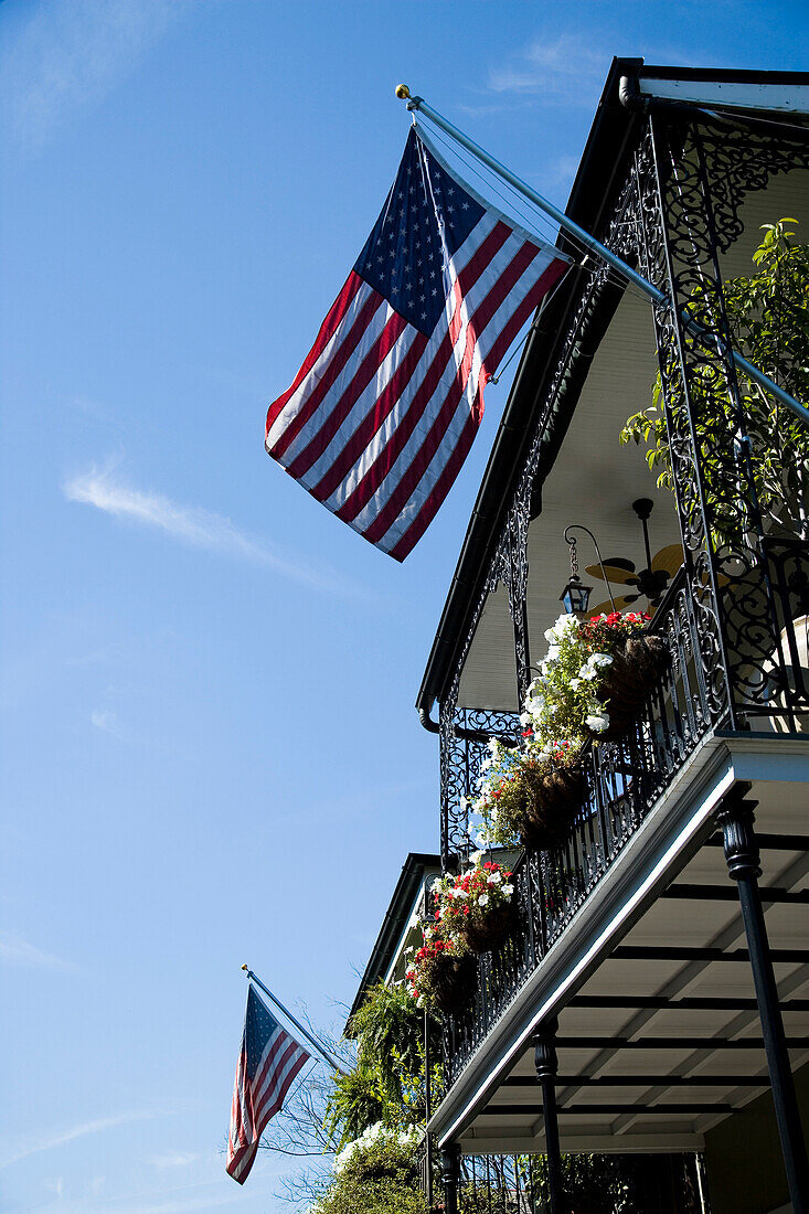 Ornate wrought iron balcony with flower hanging baskets and two US flags flying, French Quarter, New Orleans, Louisiana