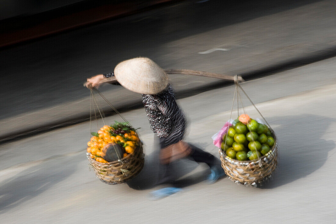 Woman carrying baskets of fruit in street, blurred motion, Hanoi, Vietnam