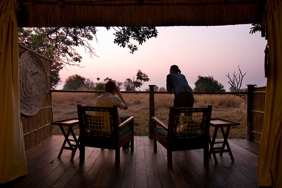 Couple looking out from room of safari lodge at dawn, South Luangwa National Park, Zambia