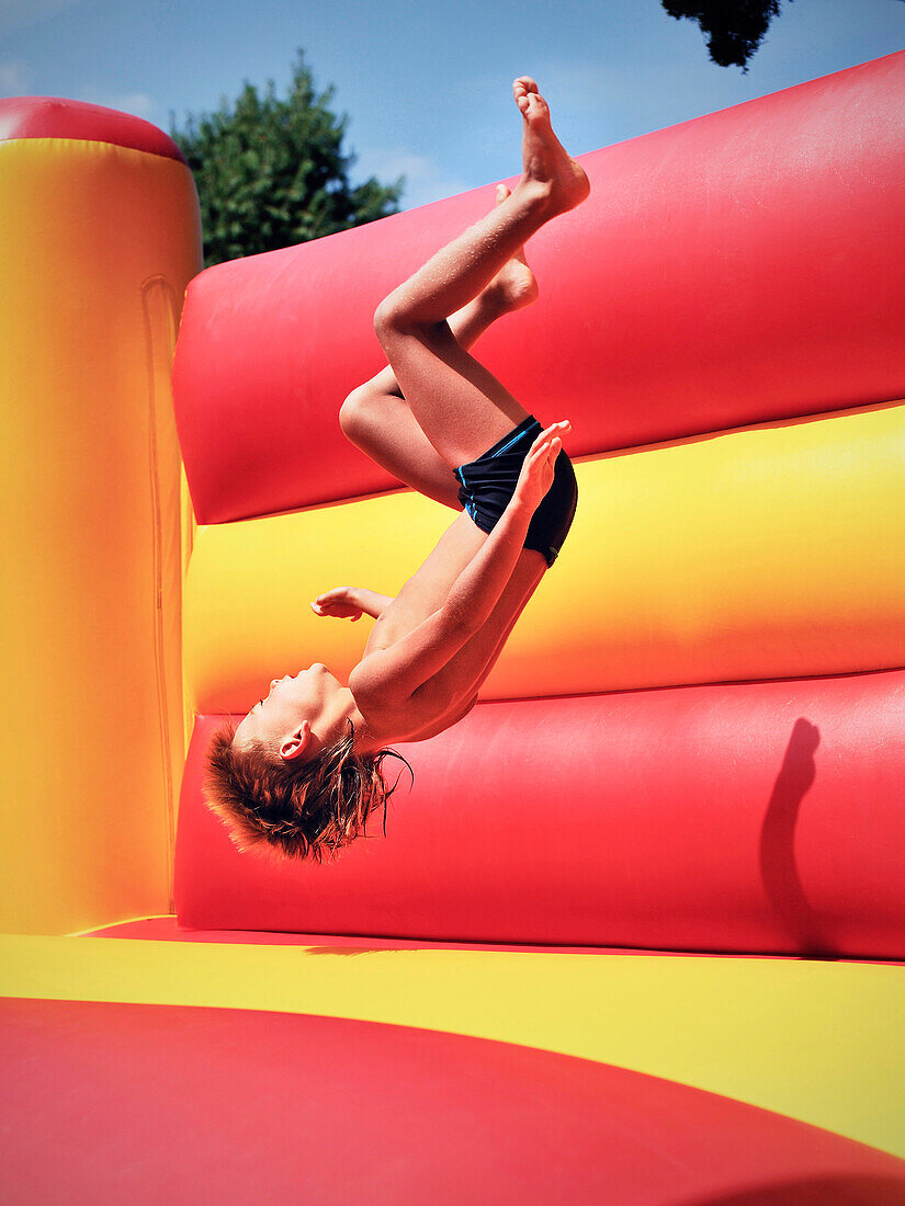 Young boy doing a somersault in a bouncy castle, Freibad Spiesel, Aalen, Schwaebische Alb, Baden-Wuerttemberg, Germany