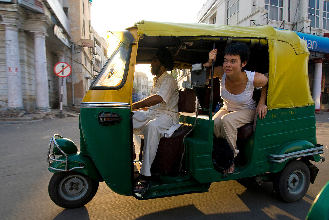 Sikh driving rickshaw with tourist leaning out the back, Delhi, India