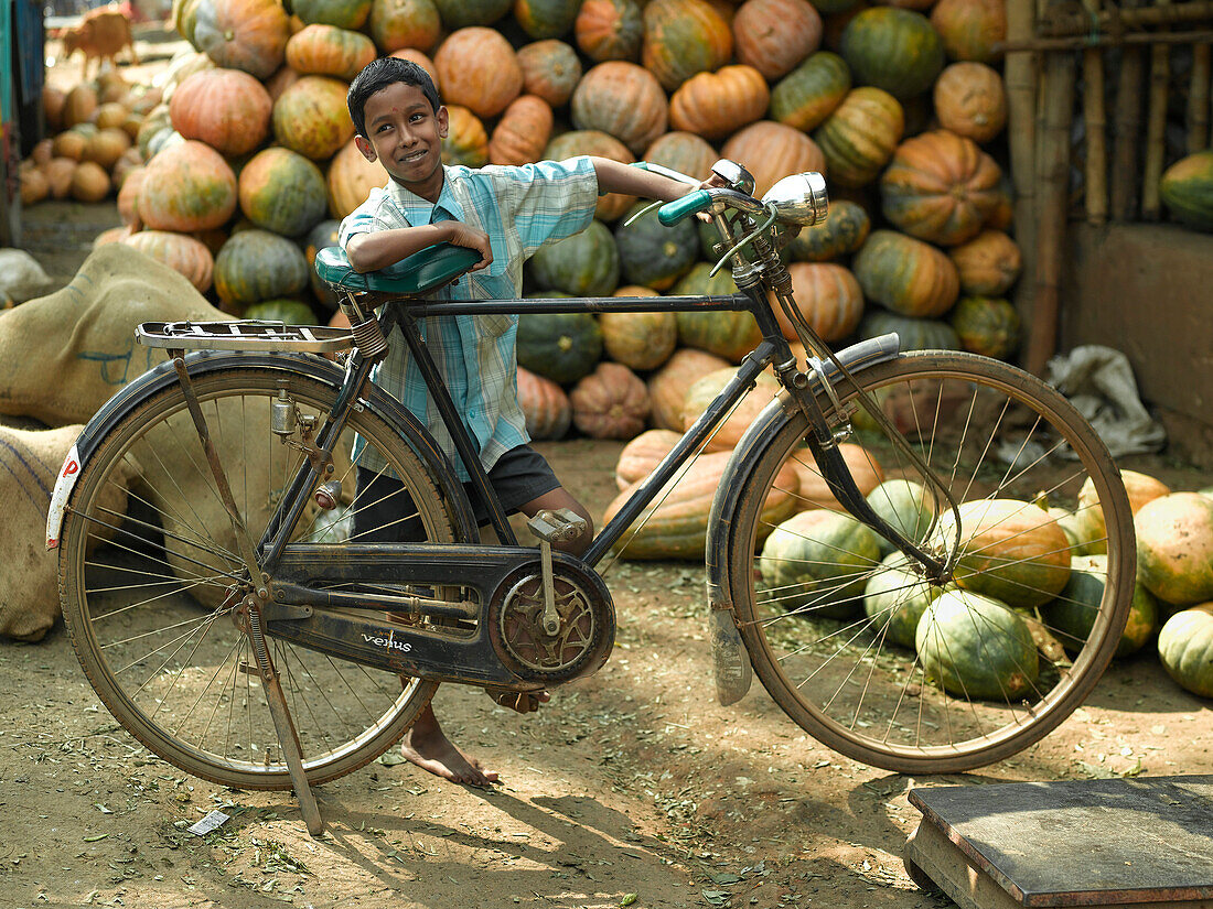 Boy leaning against bicycle infront of pumpkins, Cochin, Kerala, India
