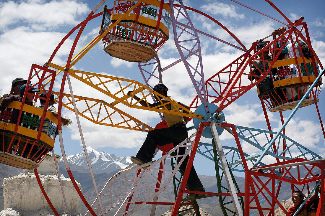 Man manually operating small ferris wheel at a fun fair in Leh, Human-powered big wheel (merry-go-round) at fun fair during the  800 year old birthday celebration of the Buddhist Drukpa Lineage, Naro Photang Shey (Shey Monastery), Leh, Ladakh, Himalayas, 