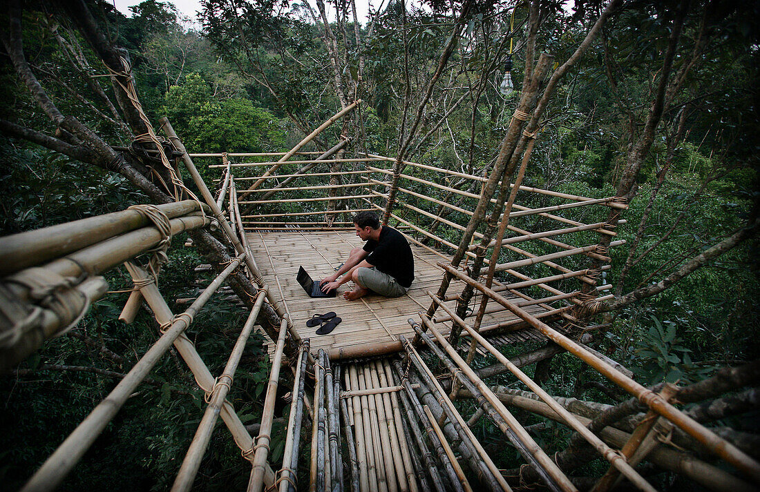 Man using a laptop in a remote tribal village on bamboo tree top canopy platform in forest, Mawlynnong, East Khasi Hills, Meghalaya, North East States, India