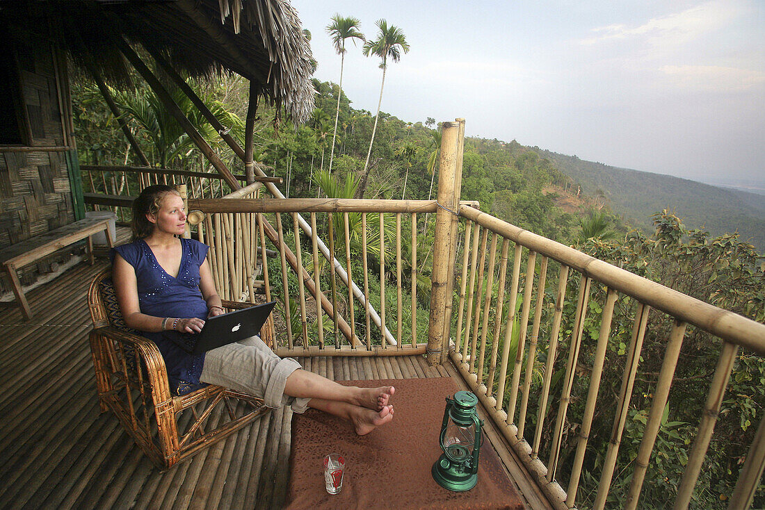 A  woman using a wireless laptop computer on the balcony of a remote bamboo hut, Near Mawlynnong, East Khasi Hills, Meghalaya, North East States, India