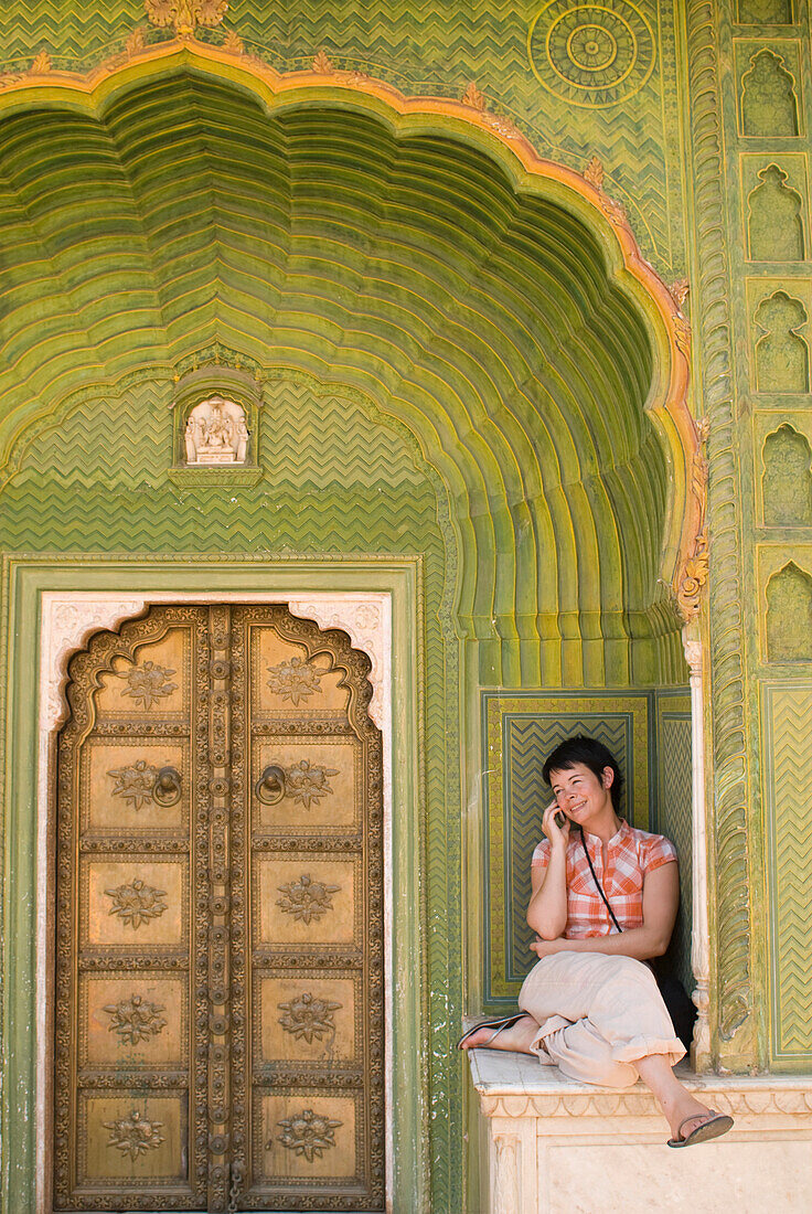Woman chatting on mobile phone in decorated entrance of the City Palace, Jaipur, Rajasthan, India