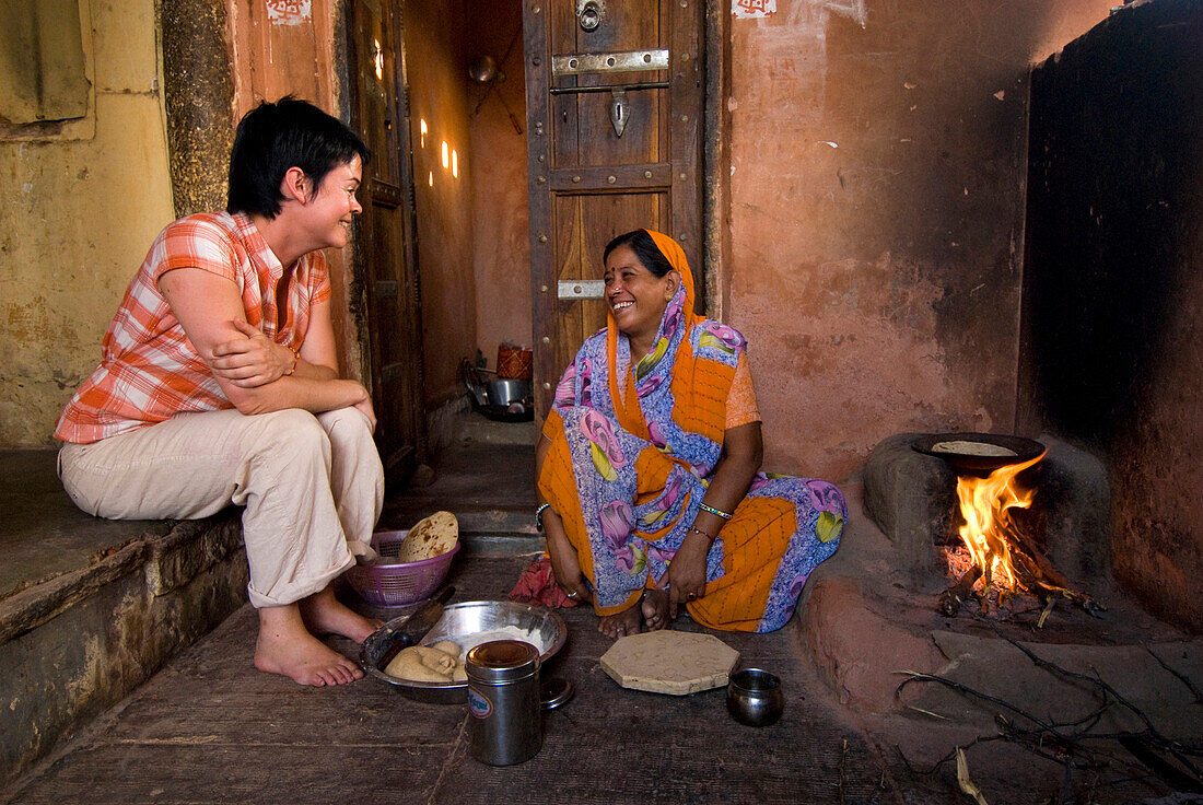 Western woman chatting with Indian lady as she cooks chapatis and prepares meal, Jaipur, Rajasthan, India
