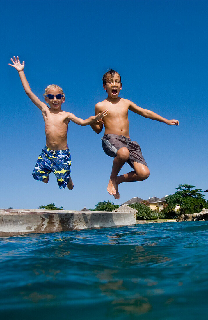 Two children jumping off platform into the sea, Discovery Bay, Jamaica