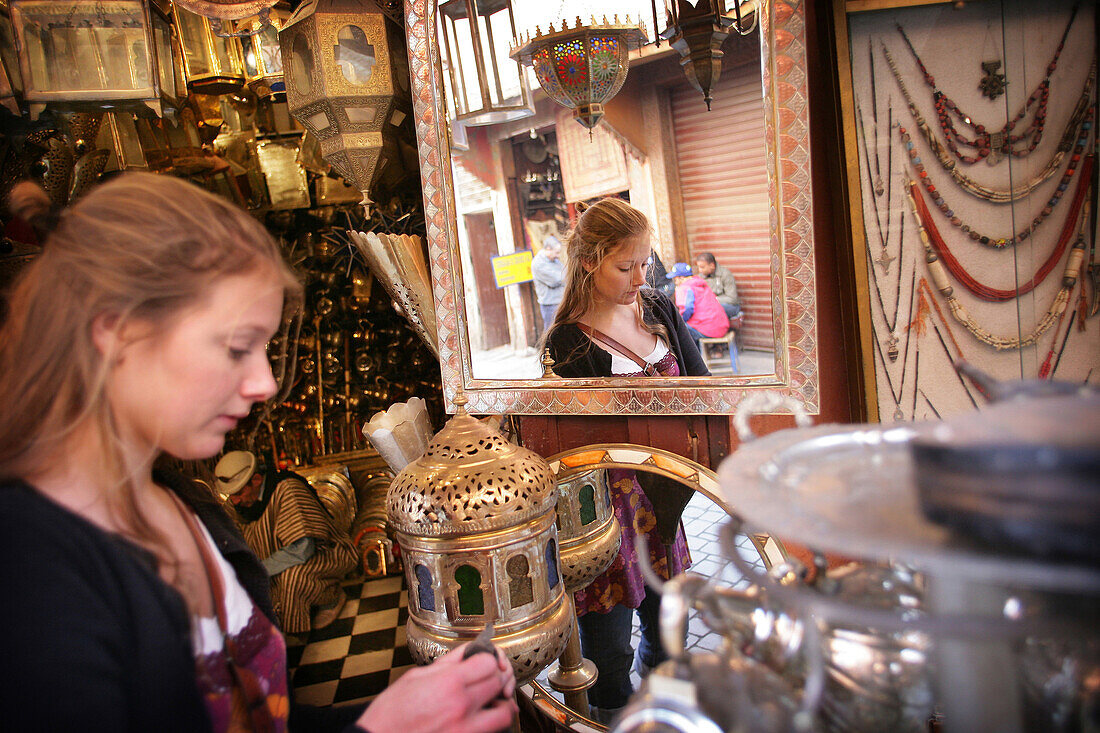 Young woman browsing for antiques in a market stall in the souk, Shopping in the Medina, Marrakesh, Morocco.
