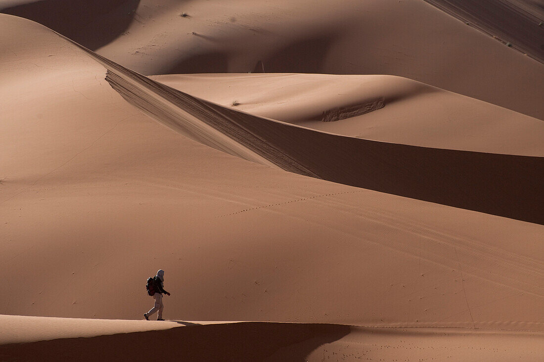 Tourist walking through sand dunes in the Erg Chebbi area of the Sahara Desert, Merzouga, Morocco.