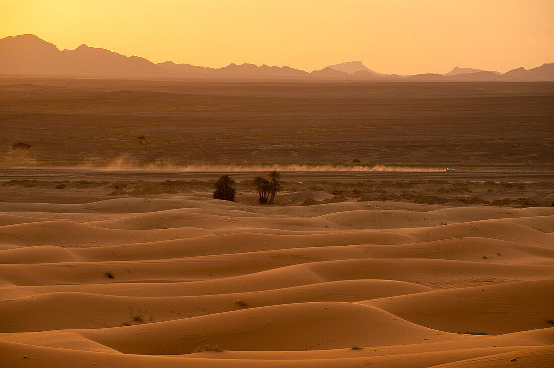 Car driving along desert road at dusk in the Erg Chebbi area of the Sahara Desert near Merzouga, Morocco, Merzouga, Morocco.