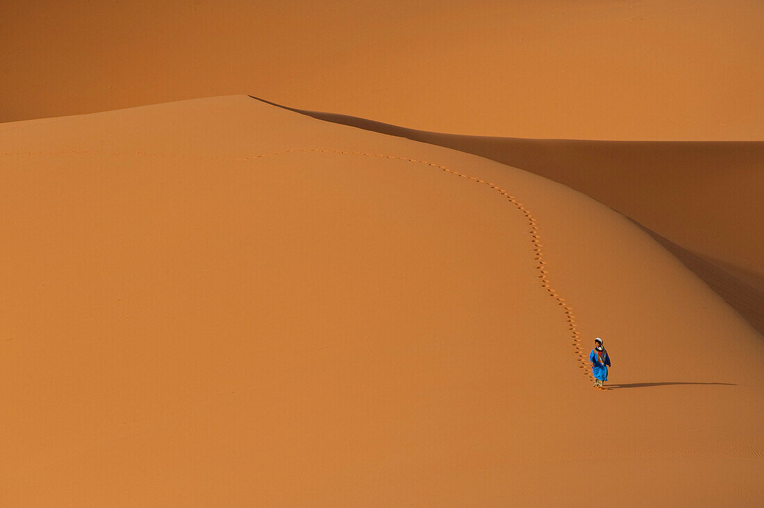 Berber walking across sand dunes in the Erg Chebbi area of the Sahara Desert, Merzouga, Morocco, Merzouga, Morocco.