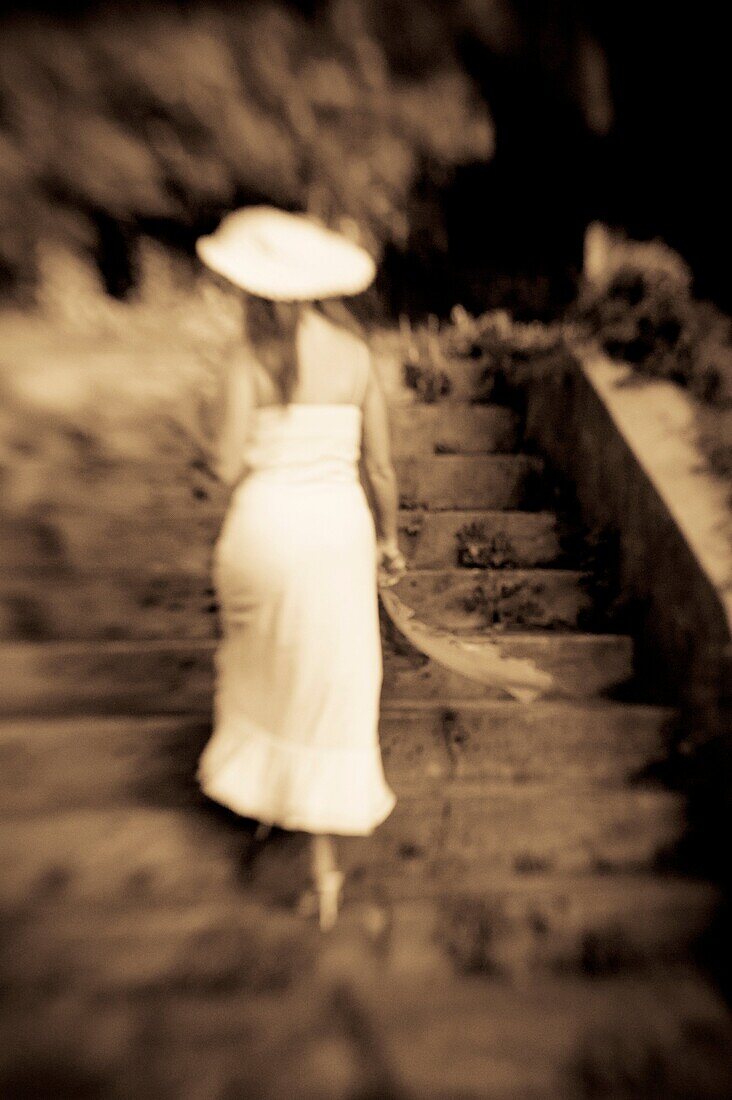 Back view of a woman in a white dress walking up a stairway, outdoors