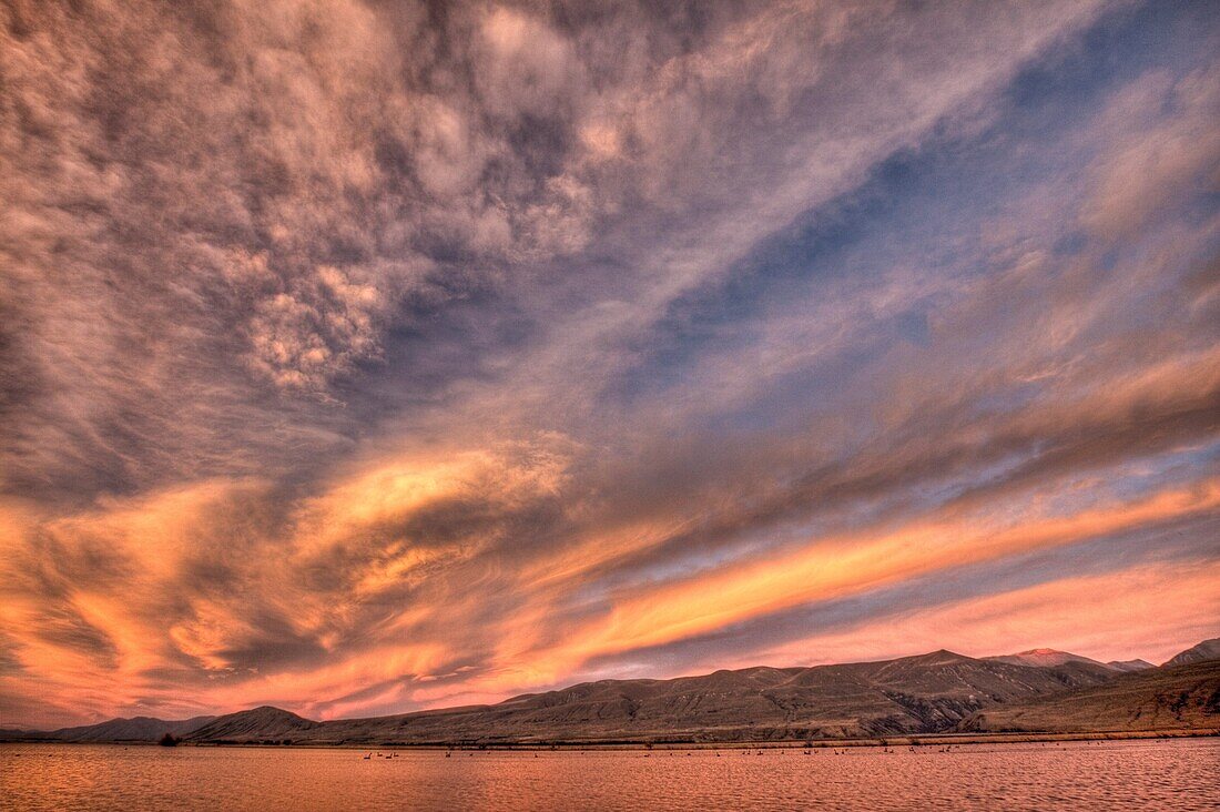 Frontal weather system from SW moves high over Lake Heron sheep & cattle station at dawn, autumn, Canterbury