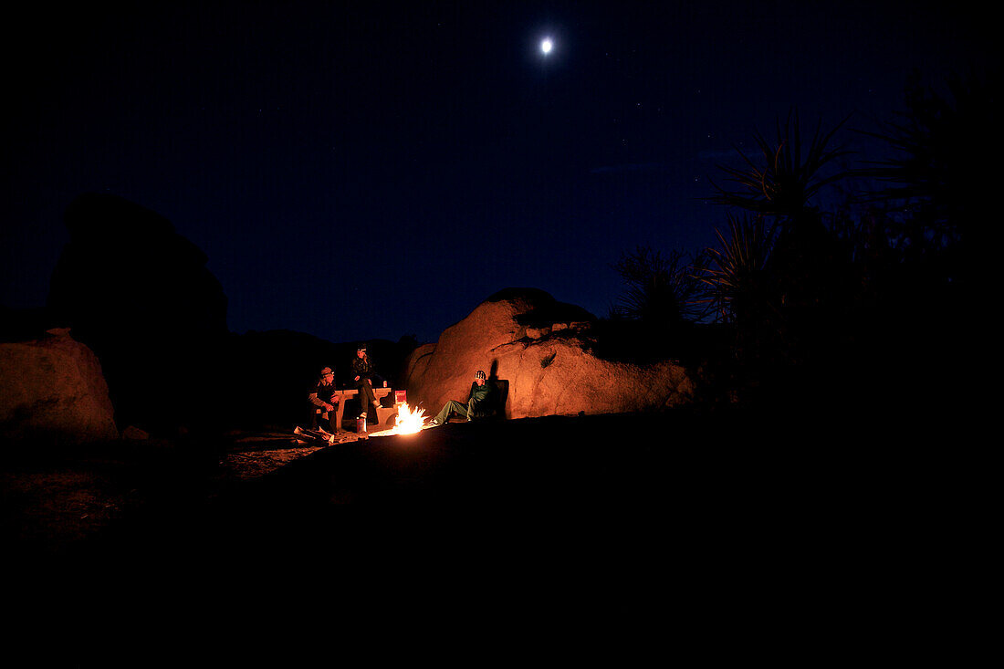 Three people sitting together around a campfire, Joshua Tree National Park, California, USA