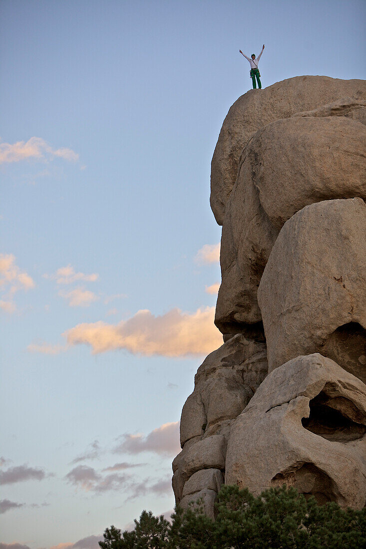 Junger Kletterer steht auf dem Gipfel eines Felsens und jubelt, Joshua Tree National Park, Kalifornien, USA