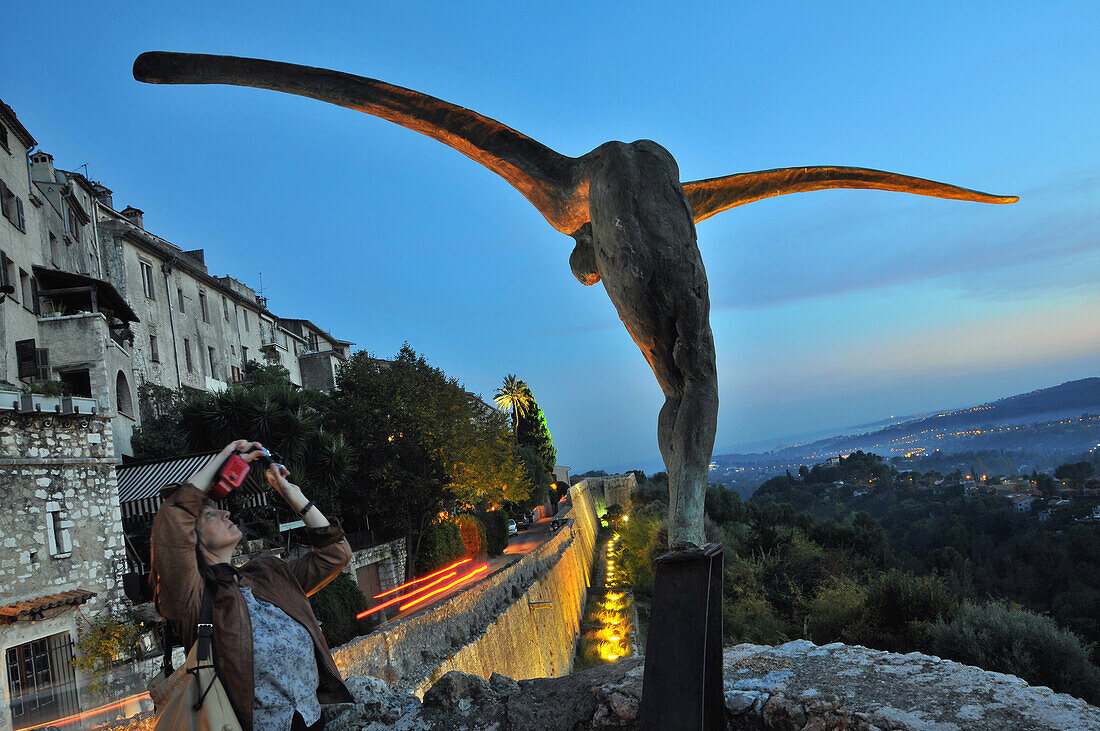 Woman taking photo of statue in the evening, Saint-Paul-de-Vence, Cote d'Azur, South France, Europe