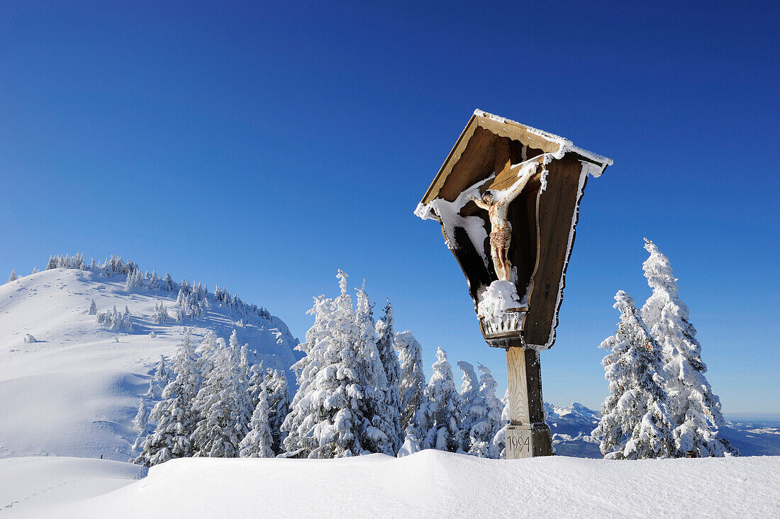 Verschneites Wegkreuz mit Winterwald im Hintergrund, Hochries, Chiemgauer Alpen, Chiemgau, Oberbayern, Bayern, Deutschland