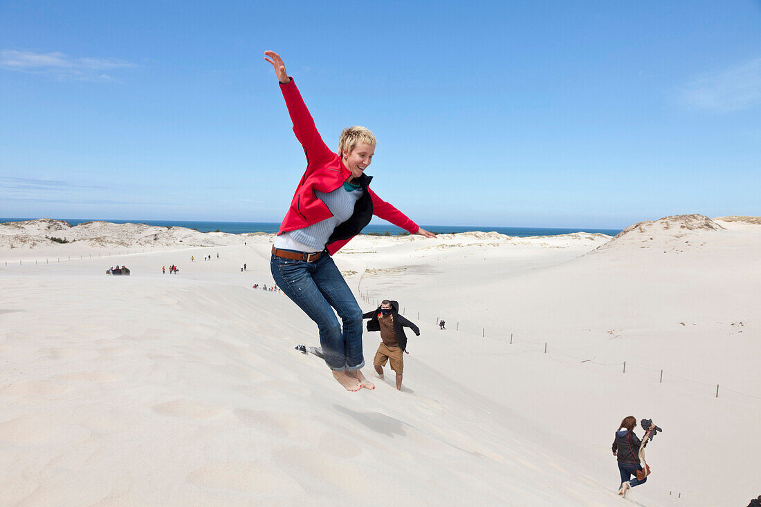 Leba Dunes, young woman jumping into the dunes, view towards the sea, UNESCO World Biosphere Reserve, Slowinski National Park, Polish Baltic Sea coast, MR, Leba, Pomeranian, Poland