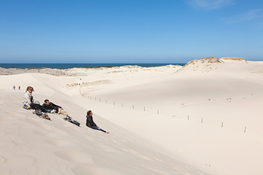 Three hikers sitting on the dunes, view towards the sea, Dunes of Leba, UNESCO World Biosphere Reserve, Slowinski National Park, Polish Baltic Sea coast, Leba, Pomeranian, Poland