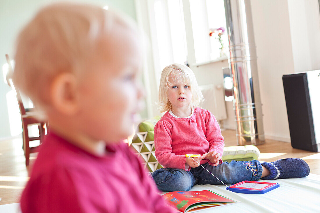 Zwei kleine Mädchen spielen im Wohnzimmer mit Spielzeug und Kinderbücher, 2 und 5 Jahre alt, MR, Leipzig, Sachsen, Deutschland