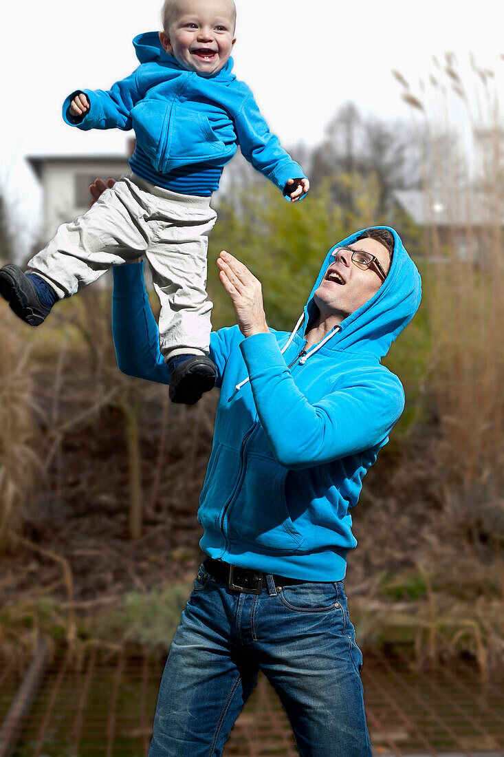 Father playing with his son in the garden, throwing him in the air, both wearing blue shirts, boy 18 months old, MR, Bad Oeynhausen, North Rhine-Westphalia, Germany
