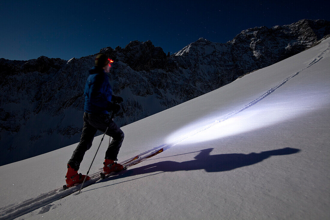 Person backcountry skiing in the moonlight with headlamp, Alpspitze, Wetterstein, Alps, Bavaria, Germany