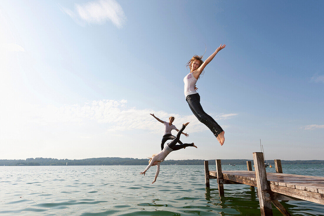 Junge Menschen springen von Bootssteg in Starnberger See, Bayern, Deutschland