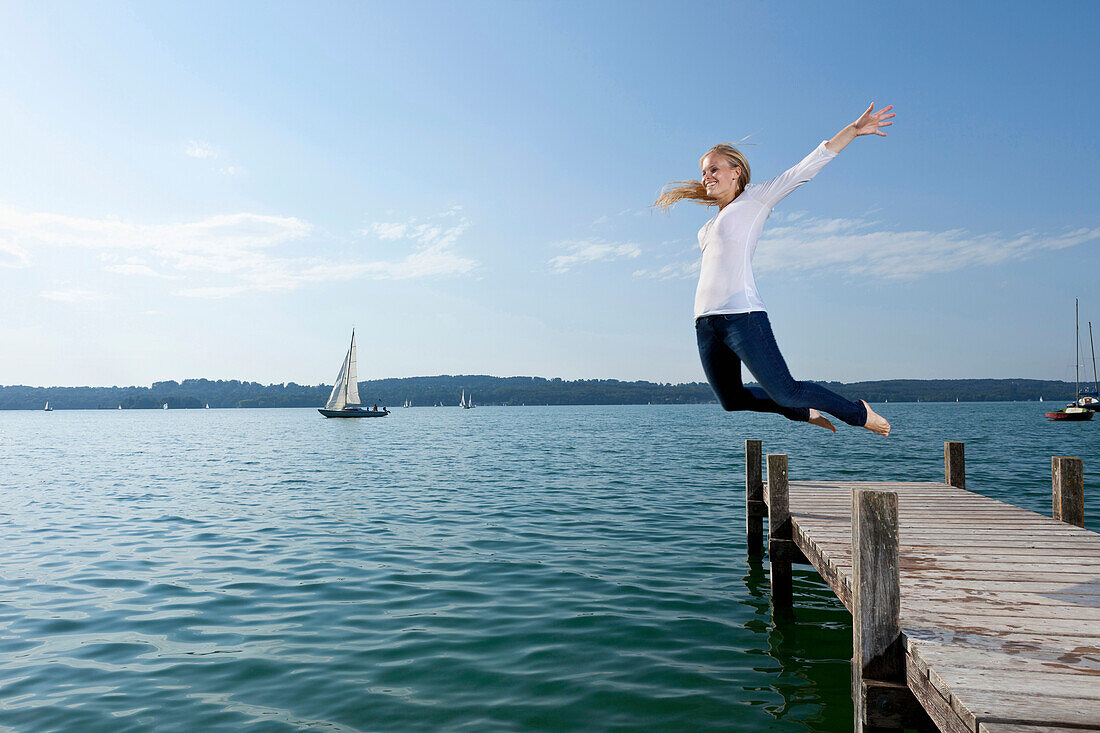 Junge Frau springt von Bootssteg in Starnberger See, Bayern, Deutschland