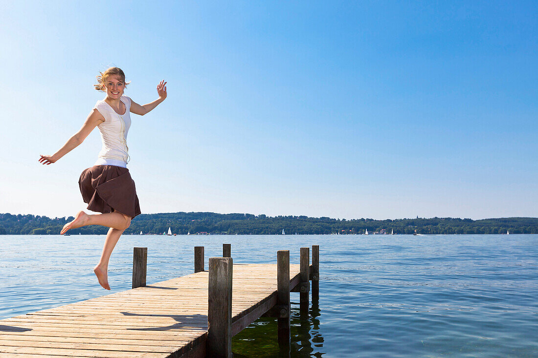 Girl jumping on the pier at Lake Starnberg, Upper Bavaria, Germany