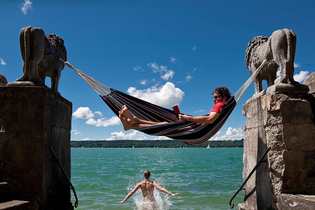 Young woman jumping into the water, man reading in hammock, Lake Starnberg, Upper Bavaria, Germany, Europe