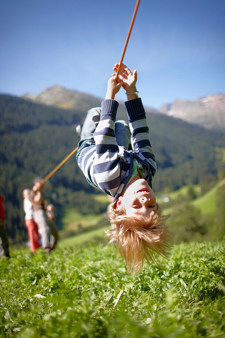 Boy hanging upside down on a rope during a hike, Pflersch, Gossensass, South Tyrol, Italy