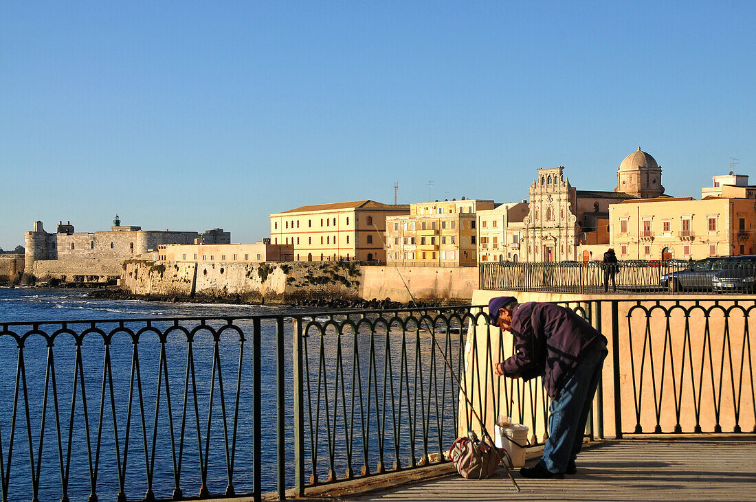 Angler with the houses of Siracusa in the background, at Lungomare, Siracusa